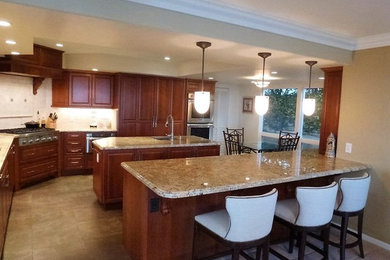 Example of a large tuscan l-shaped porcelain tile eat-in kitchen design in Hawaii with an undermount sink, raised-panel cabinets, medium tone wood cabinets, granite countertops, beige backsplash, mosaic tile backsplash, paneled appliances and an island