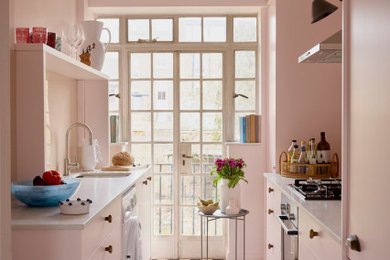 Design ideas for a bohemian galley enclosed kitchen in London with a submerged sink, flat-panel cabinets, pink cabinets, stainless steel appliances, no island, multi-coloured floors and white worktops.