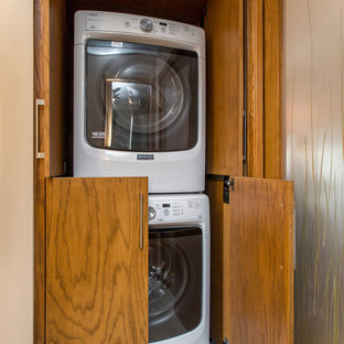 Small traditional laundry cupboard in Other with beige walls, dark hardwood flooring, flat-panel cabinets, medium wood cabinets and a stacked washer and dryer.
