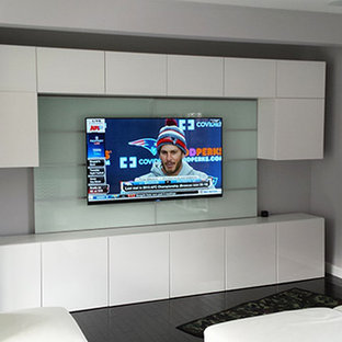 Cette photo montre une salle de cinéma moderne de taille moyenne et fermée avec un téléviseur encastré, un mur gris, un sol en bois foncé et un sol noir.