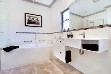 This is an example of a large contemporary master bathroom in Adelaide with open cabinets, white cabinets, a two-piece toilet, white walls, cement tiles, an integrated sink, laminate benchtops, grey floor, white benchtops, a hinged shower door, a drop-in tub, a curbless shower, black and white tile and ceramic tile.