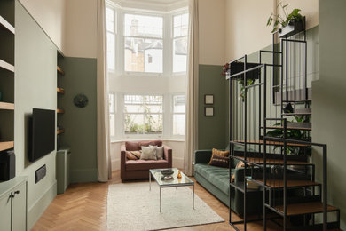 This is an example of a medium sized contemporary formal enclosed living room in London with green walls, medium hardwood flooring, a wall mounted tv, brown floors, a coffered ceiling and feature lighting.