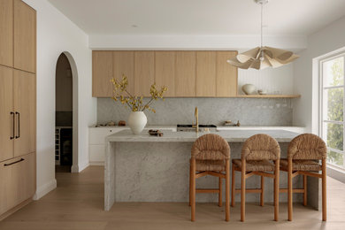 Inspiration for a beach style galley kitchen in Sydney with a farmhouse sink, flat-panel cabinets, medium wood cabinets, grey splashback, stainless steel appliances, light hardwood floors, with island, beige floor and grey benchtop.