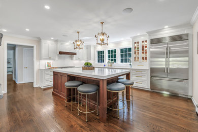 Enclosed kitchen - large traditional u-shaped medium tone wood floor and brown floor enclosed kitchen idea in New York with an integrated sink, recessed-panel cabinets, white cabinets, marble countertops, white backsplash, marble backsplash, stainless steel appliances, an island and white countertops