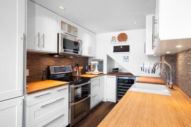 This is an example of a mid-sized transitional u-shaped eat-in kitchen in Other with a farmhouse sink, shaker cabinets, white cabinets, wood benchtops, multi-coloured splashback, stainless steel appliances, a peninsula, matchstick tile splashback, dark hardwood floors, brown floor and brown benchtop.