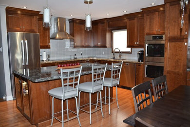 Open concept kitchen - large transitional l-shaped medium tone wood floor open concept kitchen idea in Toronto with an undermount sink, recessed-panel cabinets, dark wood cabinets, quartzite countertops, gray backsplash, glass tile backsplash, stainless steel appliances and an island