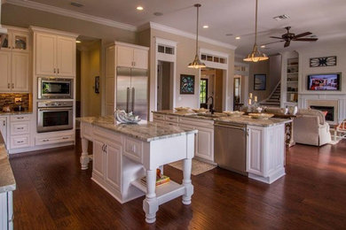 Large transitional l-shaped open plan kitchen in Tampa with an undermount sink, raised-panel cabinets, white cabinets, granite benchtops, brown splashback, matchstick tile splashback, stainless steel appliances, dark hardwood floors, multiple islands, brown floor and grey benchtop.