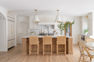 Example of a large classic u-shaped medium tone wood floor open concept kitchen design in DC Metro with a farmhouse sink, recessed-panel cabinets, white cabinets, quartz countertops, white backsplash, subway tile backsplash, paneled appliances, an island and white countertops
