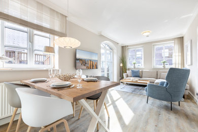 Offenes Skandinavisches Wohnzimmer ohne Kamin mit beiger Wandfarbe, hellem Holzboden, TV-Wand und grauem Boden