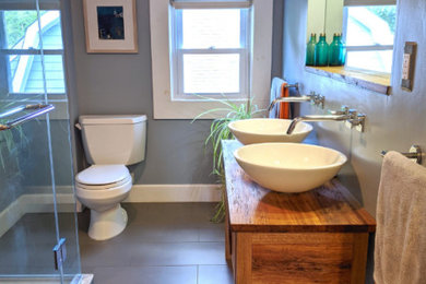 Small trendy 3/4 gray tile and porcelain tile porcelain tile, gray floor and double-sink corner shower photo in New York with flat-panel cabinets, dark wood cabinets, a two-piece toilet, blue walls, a vessel sink, wood countertops, a hinged shower door, brown countertops and a freestanding vanity