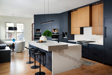 Mid-sized trendy medium tone wood floor and brown floor eat-in kitchen photo in Dallas with flat-panel cabinets, blue cabinets, concrete countertops, white backsplash, marble backsplash, paneled appliances, an island and gray countertops