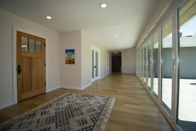Ejemplo de puerta principal moderna grande con paredes beige, suelo de madera clara, puerta simple, puerta de madera clara y suelo multicolor