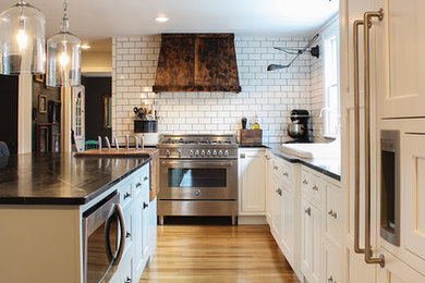 Country l-shaped medium tone wood floor kitchen photo in Boston with recessed-panel cabinets, white cabinets, soapstone countertops, white backsplash, subway tile backsplash, paneled appliances and an island