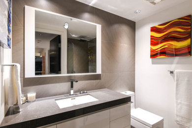 Mid-sized trendy master brown tile and porcelain tile porcelain tile, gray floor and single-sink walk-in shower photo in Vancouver with flat-panel cabinets, white cabinets, a wall-mount toilet, white walls, an undermount sink, quartz countertops, a hinged shower door, gray countertops and a floating vanity