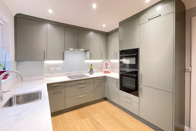 This is an example of a small modern u-shaped kitchen in Edinburgh with a built-in sink, flat-panel cabinets, green cabinets, quartz worktops, white splashback, glass sheet splashback, black appliances and white worktops.