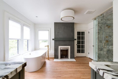 This is an example of a large contemporary master bathroom in Oklahoma City with shaker cabinets, grey cabinets, a freestanding tub, a corner shower, white tile, marble, white walls, light hardwood floors, an undermount sink, marble benchtops, beige floor, a hinged shower door and grey benchtops.