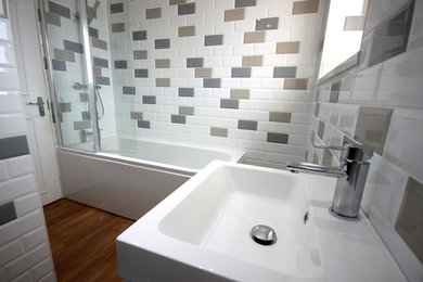 Mid-sized contemporary kids bathroom in Other with furniture-like cabinets, white cabinets, a corner tub, a shower/bathtub combo, a one-piece toilet, multi-coloured tile, ceramic tile, white walls, laminate floors, an integrated sink and brown floor.