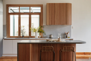 Inspiration for a mid-sized midcentury l-shaped eat-in kitchen in Adelaide with an undermount sink, flat-panel cabinets, black cabinets, solid surface benchtops, grey splashback, stone slab splashback, panelled appliances, light hardwood floors, with island, brown floor and grey benchtop.