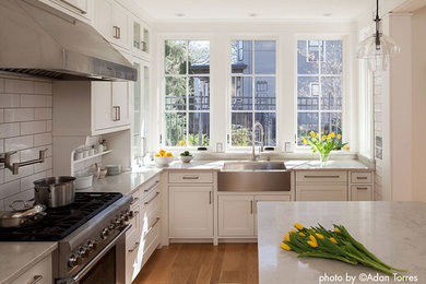 Large traditional u-shaped kitchen in Minneapolis with white splashback, subway tile splashback, stainless steel appliances, medium hardwood floors, with island, white cabinets, quartz benchtops, a farmhouse sink and recessed-panel cabinets.