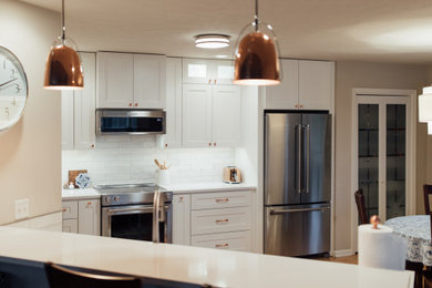 Inspiration for a mid-sized transitional u-shaped medium tone wood floor and brown floor eat-in kitchen remodel in Other with shaker cabinets, white cabinets, white backsplash, subway tile backsplash, stainless steel appliances, a peninsula and white countertops