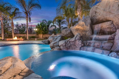 Large traditional backyard custom-shaped pool in Orange County with a water slide and concrete pavers.