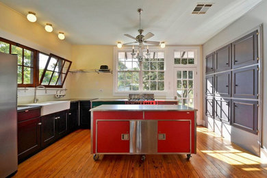 Eat-in kitchen - mid-sized country l-shaped medium tone wood floor and brown floor eat-in kitchen idea in Austin with a farmhouse sink, shaker cabinets, black cabinets, stainless steel countertops, yellow backsplash, window backsplash, stainless steel appliances, an island and black countertops