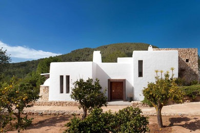 White and small mediterranean split-level clay house exterior in London with a flat roof.