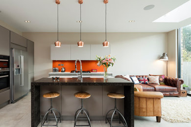 This is an example of a contemporary galley open plan kitchen in London with flat-panel cabinets, grey cabinets, orange splashback, stainless steel appliances, with island and grey floor.