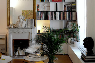Cette image montre un salon minimaliste de taille moyenne et ouvert avec une bibliothèque ou un coin lecture, un mur blanc, parquet clair, une cheminée standard, un manteau de cheminée en pierre, aucun téléviseur et un sol beige.