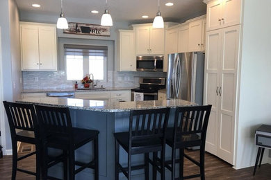 Kitchen - mid-sized traditional l-shaped medium tone wood floor and brown floor kitchen idea in Omaha with an undermount sink, shaker cabinets, white cabinets, granite countertops, gray backsplash, matchstick tile backsplash, stainless steel appliances and an island