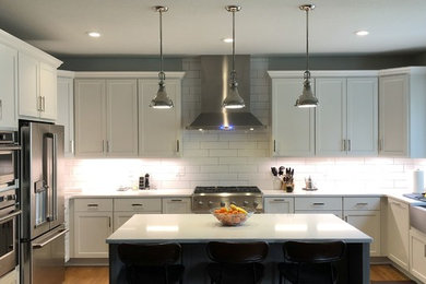 This is an example of a large transitional u-shaped eat-in kitchen in Kansas City with a farmhouse sink, shaker cabinets, grey cabinets, quartzite benchtops, white splashback, subway tile splashback, stainless steel appliances, light hardwood floors, with island, brown floor and grey benchtop.