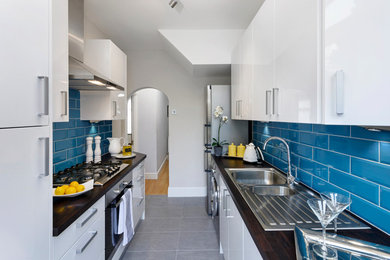 Inspiration for a small modern galley separate kitchen in London with a double-bowl sink, flat-panel cabinets, white cabinets, wood benchtops, blue splashback, ceramic splashback, stainless steel appliances, porcelain floors and no island.