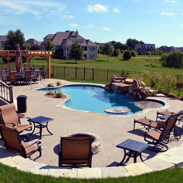 Free form pool with stone table, sun shelf, water feature, and outdoor kitchen,