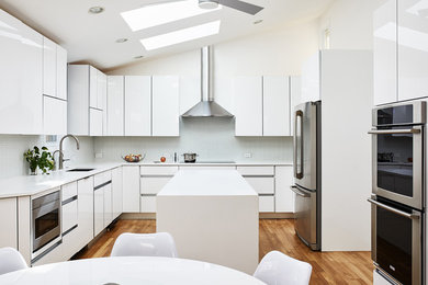 Example of a large trendy u-shaped medium tone wood floor kitchen design in DC Metro with flat-panel cabinets, white cabinets, stainless steel appliances, an island and white countertops