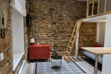 Exemple d'un petit salon mansardé ou avec mezzanine tendance avec sol en stratifié, aucune cheminée, un téléviseur fixé au mur, un sol gris et un mur en pierre.