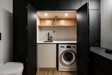 Large contemporary laundry room in Melbourne with a single-bowl sink, black cabinets, solid surface benchtops, white walls, porcelain floors and black benchtop.