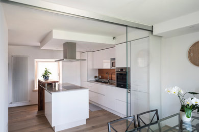 This is an example of a small contemporary l-shaped open plan kitchen in Other with with island, a double-bowl sink, flat-panel cabinets, white cabinets, quartzite benchtops, brown splashback, timber splashback, stainless steel appliances, light hardwood floors, brown floor and grey benchtop.