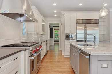 Inspiration for a large transitional light wood floor and brown floor kitchen remodel in Other with white cabinets, white backsplash, stainless steel appliances, an island, an undermount sink, shaker cabinets, marble countertops and subway tile backsplash