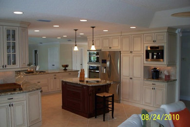 Photo of a large traditional u-shaped open plan kitchen in Miami with an undermount sink, louvered cabinets, white cabinets, granite benchtops, beige splashback, ceramic splashback, stainless steel appliances, ceramic floors and with island.