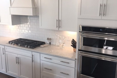 Large trendy l-shaped dark wood floor kitchen photo in Columbus with shaker cabinets, white cabinets, quartzite countertops, white backsplash, subway tile backsplash, stainless steel appliances and an island