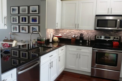 Example of a mid-sized trendy l-shaped medium tone wood floor eat-in kitchen design in Orlando with an undermount sink, shaker cabinets, white cabinets, stainless steel appliances, gray backsplash, no island, solid surface countertops and stone tile backsplash