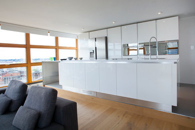 Réalisation d'une grande cuisine américaine parallèle design avec un évier encastré, un placard à porte plane, des portes de placard blanches, un plan de travail en surface solide, un électroménager en acier inoxydable, îlot et un sol gris.
