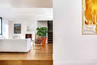 Transitional open concept living room in Paris with a library, light hardwood floors and a standard fireplace.