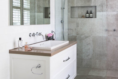 Inspiration for a mid-sized traditional master bathroom in Melbourne with recessed-panel cabinets, white cabinets, a drop-in tub, an alcove shower, a two-piece toilet, white tile, ceramic tile, white walls, ceramic floors, a drop-in sink, engineered quartz benchtops, grey floor, an open shower and brown benchtops.