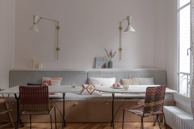 Cette image montre une salle à manger design avec une banquette d'angle, un mur blanc, un sol en bois brun et un sol marron.