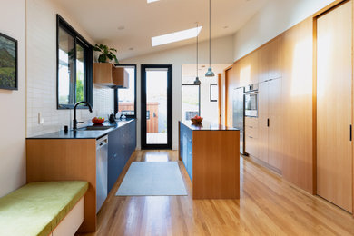 Eat-in kitchen - mid-sized modern galley medium tone wood floor and vaulted ceiling eat-in kitchen idea with flat-panel cabinets, solid surface countertops, white backsplash, an island and black countertops