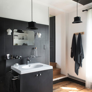 Mittelgroßes Stilmix Badezimmer En Suite mit schwarzen Schränken, schwarzen Fliesen, weißer Wandfarbe, Mineralwerkstoff-Waschtisch, weißer Waschtischplatte, flächenbündigen Schrankfronten, braunem Holzboden, Waschtischkonsole und braunem Boden in Sonstige