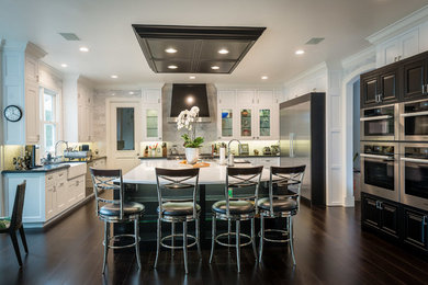 Photo of a large traditional l-shaped eat-in kitchen in Los Angeles with a farmhouse sink, recessed-panel cabinets, white cabinets, quartzite benchtops, white splashback, stone tile splashback, stainless steel appliances, dark hardwood floors and with island.