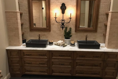 Mid-sized tuscan master beige tile and stone tile dark wood floor and brown floor bathroom photo in Phoenix with raised-panel cabinets, dark wood cabinets, a one-piece toilet, beige walls, a vessel sink, marble countertops and a hinged shower door