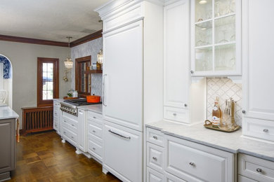 Mid-sized transitional galley medium tone wood floor and brown floor eat-in kitchen photo in Seattle with a farmhouse sink, raised-panel cabinets, white cabinets, marble countertops, gray backsplash, marble backsplash, stainless steel appliances and an island